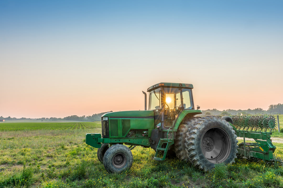 Image of a tractor in a field with the sun low on the horizon